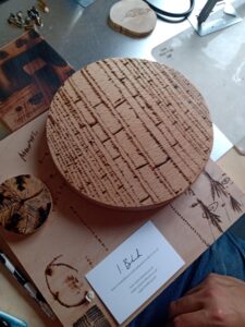 An example of work. A round wooden board decorated with lines to look like a tree, sits on top of some other examples